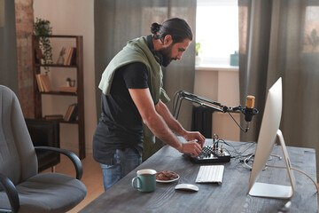 Medium long shot of young man adjusting audio mixer setting sound in home studio before starting online streaming © Mediaphotos