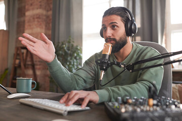 Horizontal medium portrait of handsome young Middle Eastern man wearing headphones sitting at desk...