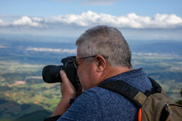 Homem fotografando natureza de cima da montanha