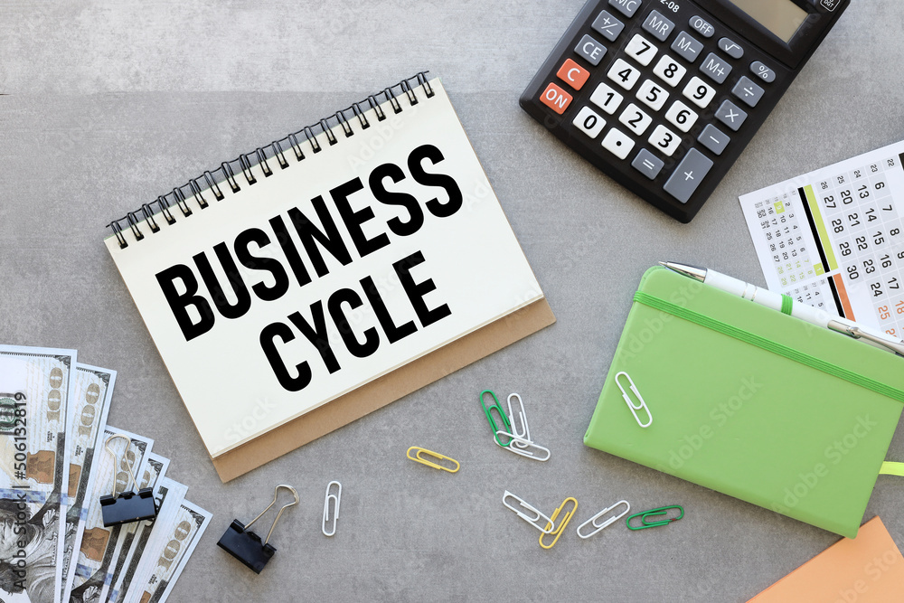 Poster business cycle. open notepad on gray background near green notepad and calculator