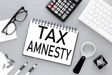 TAX AMNESTY notepad on gray background near white keyboard and calculator