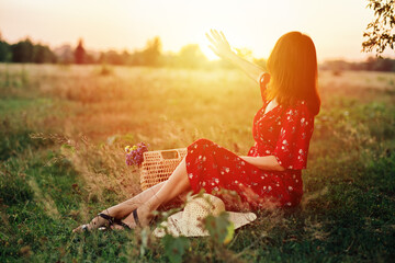 Sun and womens health, vitamin D and summer sun. Back view woman on sunset in nature background. Young woman in dress on field under sunset light.