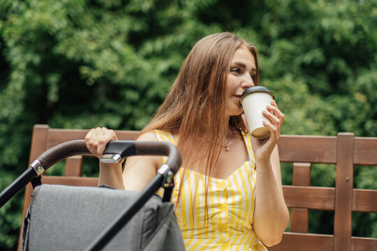 Caffeine And Breastfeeding. Young Mom With Coffee To Go Cup Walk With Newborn Son. Mother Walk With Newborn Baby In Stroller While Drinking Take Away Coffee.