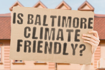 The question " Is Baltimore climate-friendly? " is on a banner in men's hands with blurred background. Support. Team. Activist. Urban. Sunset. Carbon. Ecology. Energy. New. Clean. Warming. Waste