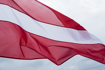 Latvian flag waving in wind. Flag of Latvia on cloudy white sky background.  - obrazy, fototapety, plakaty