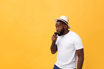 young handsome african american boy singing emotional with microphone isolated on yellow...