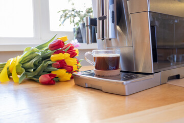 Cup of coffee with milk and tulips flowers on wooden kitchen table. Freshly brewed cappuccino...