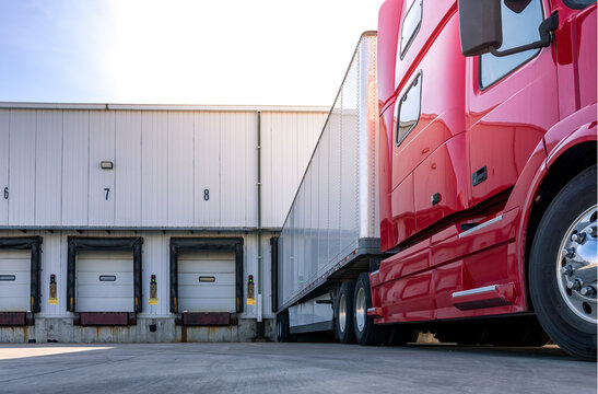 Red modern American semi truck parked at the docks, waiting to get loaded. Shipping and receiving, transportation business concept. Truck driving jobs.
