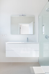 Part of a modern bathroom. A view of a white cabinet with a sink and a glass shower cubicle. - 506138052