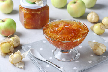 Homemade transparent jam physalis and apples in bowl and glass jar on gray background