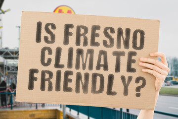 The question " Is Fresno climate-friendly? " is on a banner in men's hands with blurred background. Support. Team. Activist. Urban. Sunset. Carbon. Ecology. Energy. New. Clean. Warming. Waste