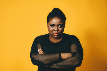 portrait of a thoughtful black woman with crossed arms on yellow background studio