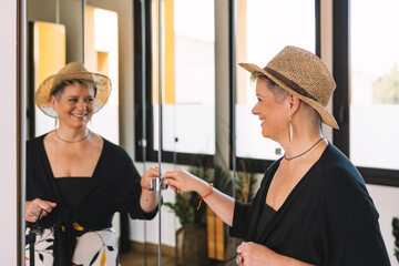 mature woman traveller, looking at herself in the mirror as she dresses to go for a walk along the coast on her summer holiday.