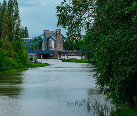 niebieski most nad rzeką zielone drzewa nad wodą - obrazy, fototapety, plakaty