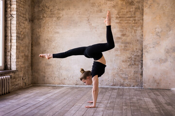 Young girl teenager doing stretching in gym. Blond woman gymnast ballerina in black sportswear dancing. Girl doing acrobatic figures and string. Girl standing on hands