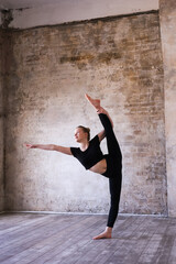 Young girl teenager doing stretching in gym. Blond woman gymnast ballerina in black sportswear dancing. Girl doing acrobatic figures and string. Girl standing on hands