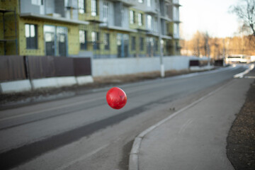 Red balloon flies over road. Object is in air. Color contrast.