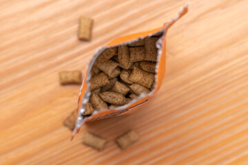 Open package of dry dog and cat treats viewed from above on a wooden table. Pet food.