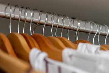 Different clothes on hangers close up. Clothes hanger rod chrome, selective focus, closet organization, wooden hangers.