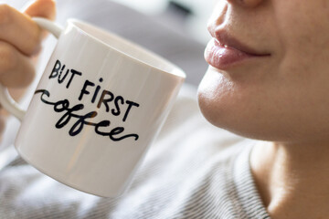 "but first, coffee" handwritten mug with smiling woman drinking coffee. close up.
