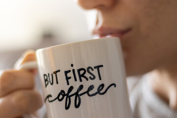 "but first, coffee" handwritten mug with smiling woman drinking coffee. close up.