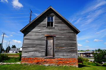 An old abandoned vintage wooden home sits on a hillside in Ripon, Wisconsin during beautiful cloudy July weather.