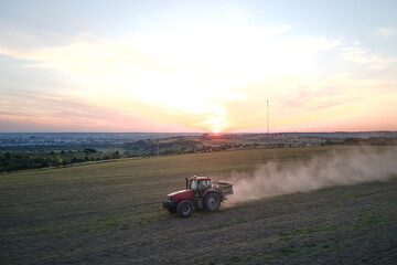 Tractor spraying fertilizers with insecticide herbicide chemicals on agricultural field at sunset