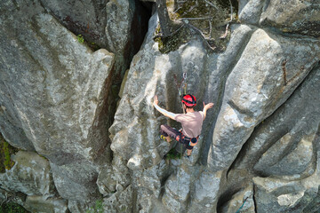 Young man climbing steep wall of rocky mountain. Male climber overcomes challenging route. Engaging...