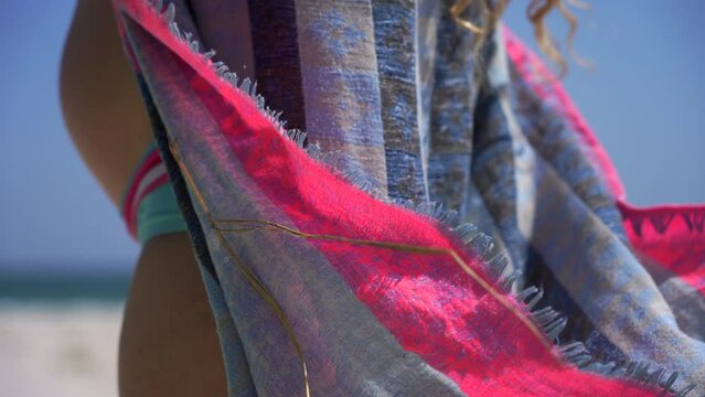 A pregnant curly-haired girl in a swimsuit ties a pareo against the backdrop of the sea on a sunny day. big tummy on the background of the blue sea. motherhood