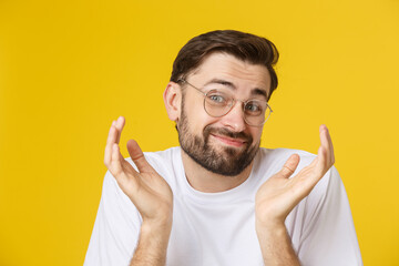 Closeup of young handsome man looking and showing funny face at camera, wearing glass. Isolated view on yellow background.