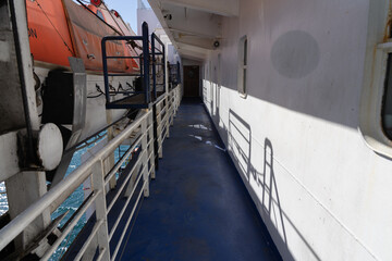 Exterior corridor of ship with railings and emergency lifeboats