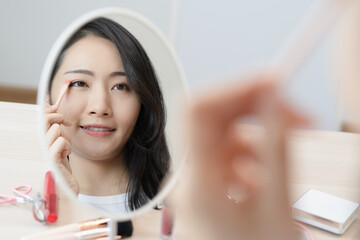 Daily makeup routine, Asian young women looks in the mirror during putting eyeshadow on her eyes.