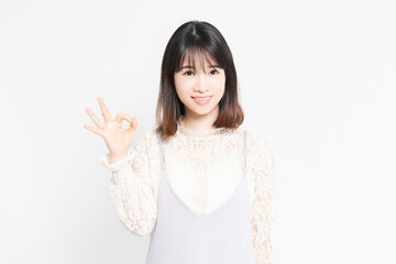 白い背景の前でOKのポーズをする若い女性