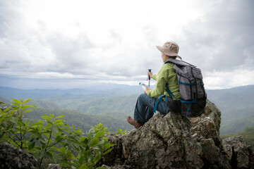 Young female tourist with backpack relaxing on top rock and enjoying view of mountains