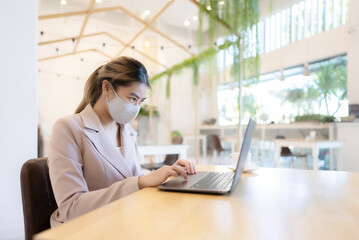 Asian business woman wear face mask protective and working on computer laptop in cafe. New normal, Covid-19 and pandemic concept