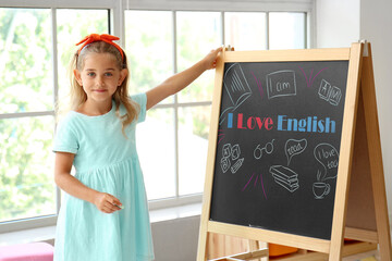 Cute little girl near chalkboard with text I LOVE ENGLISH