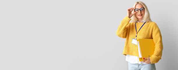 Portrait of mature woman holding folder on light background with space for text