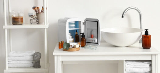 Sink, small open refrigerator for cosmetics and bath accessories in light bathroom