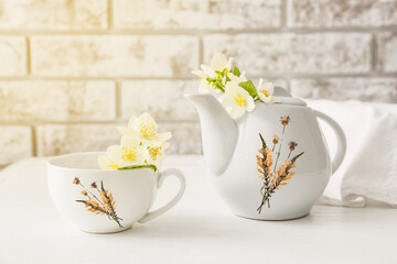 Stylish teapot and cup with beautiful flowers on table against brick wall