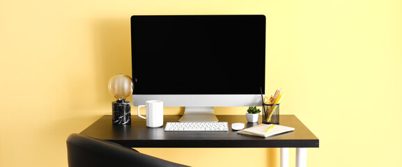 Workplace with modern computer near yellow wall