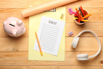 Composition with blank to do list, stationery, headphones and piggy bank on wooden background