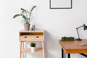 Standing desk with houseplants and wooden table with mobile phone and notebook near light wall