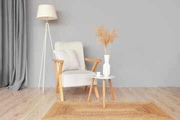 Table with vase, cup of coffee, armchair and standard lamp near grey wall