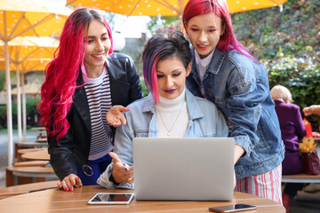 Beautiful women with bright hair using laptop at table in street cafe