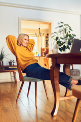 Relaxed woman sitting at dinning table at home looking on laptop screen