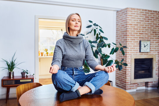 Middle aged woman sitting on a table at home relaxing meditating