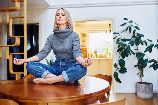 Mature woman meditating while sitting on a table at home
