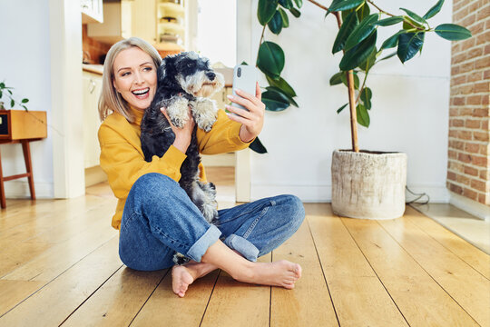 Happy middle aged woman takes selfie with dog at home