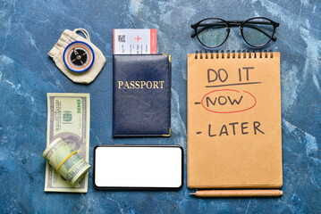 Notebook with text DO IT NOW, passport with ticket, money and compass on blue background