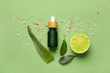 Bottle of natural serum with sea salt, plant leaves and lime on green background